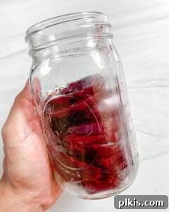 Small Batch Pickled Beets neatly arranged in a mason jar against a white background, before the brine is added.