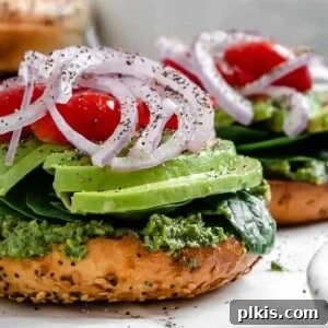 Completed Vegan Bagel Sandwich with Pesto on a white surface and another sandwich in the background