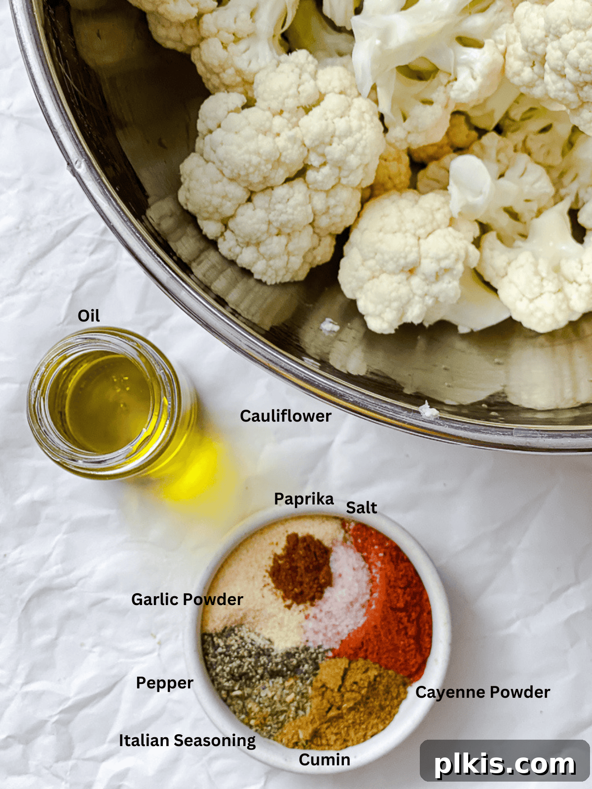 Fiery Roasted Cauliflower 3 Ingredients for Spicy Roasted Cauliflower measured out on a white surface, including cauliflower florets, olive oil, and various spices.