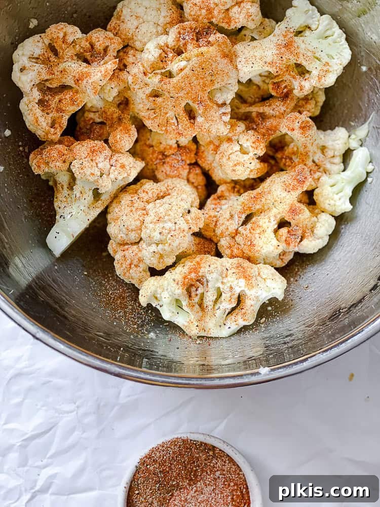 Fiery Roasted Cauliflower 5 Process shot showing cauliflower florets being tossed with spices in a large bowl.