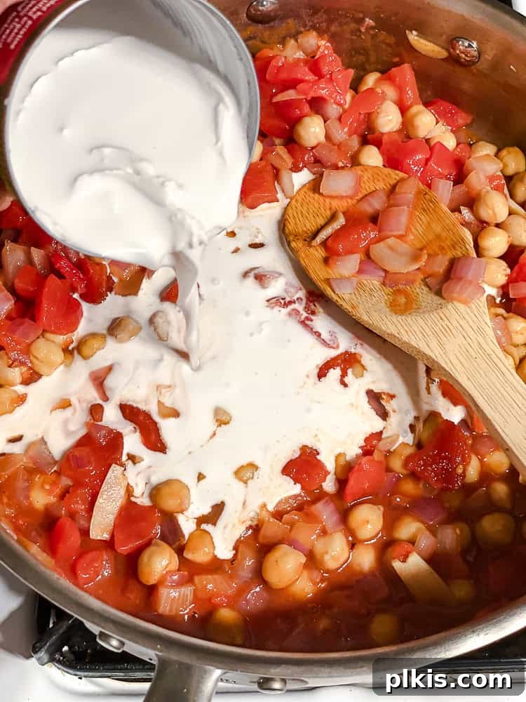 Effortless Eggplant Curry 6 Creamy coconut milk being poured into the pan with the sautéed aromatics and spices