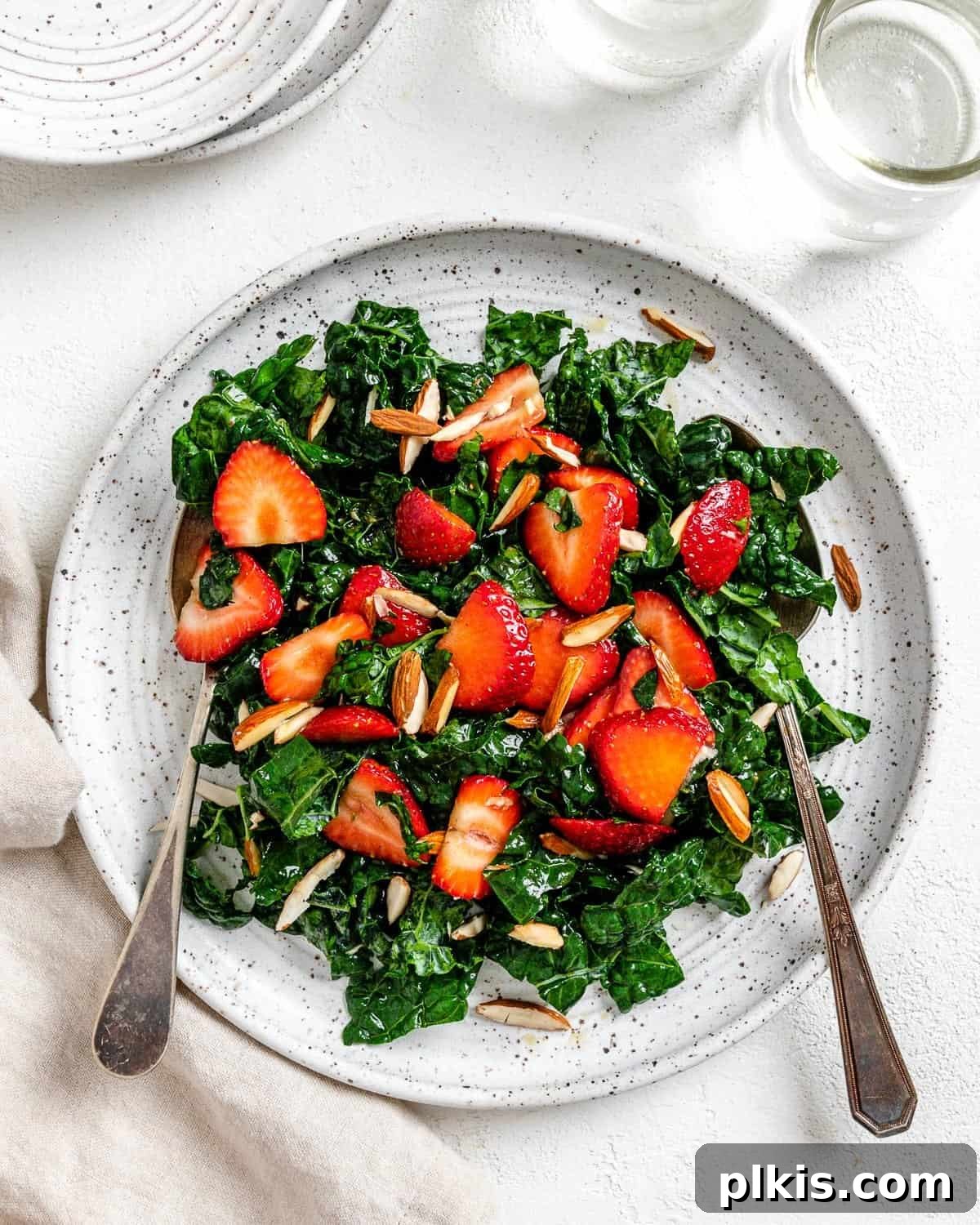 Berry Burst Kale Salad 2 completed Strawberry Kale Salad on a white plate against a white surface, showcasing fresh strawberries, green kale, and almonds