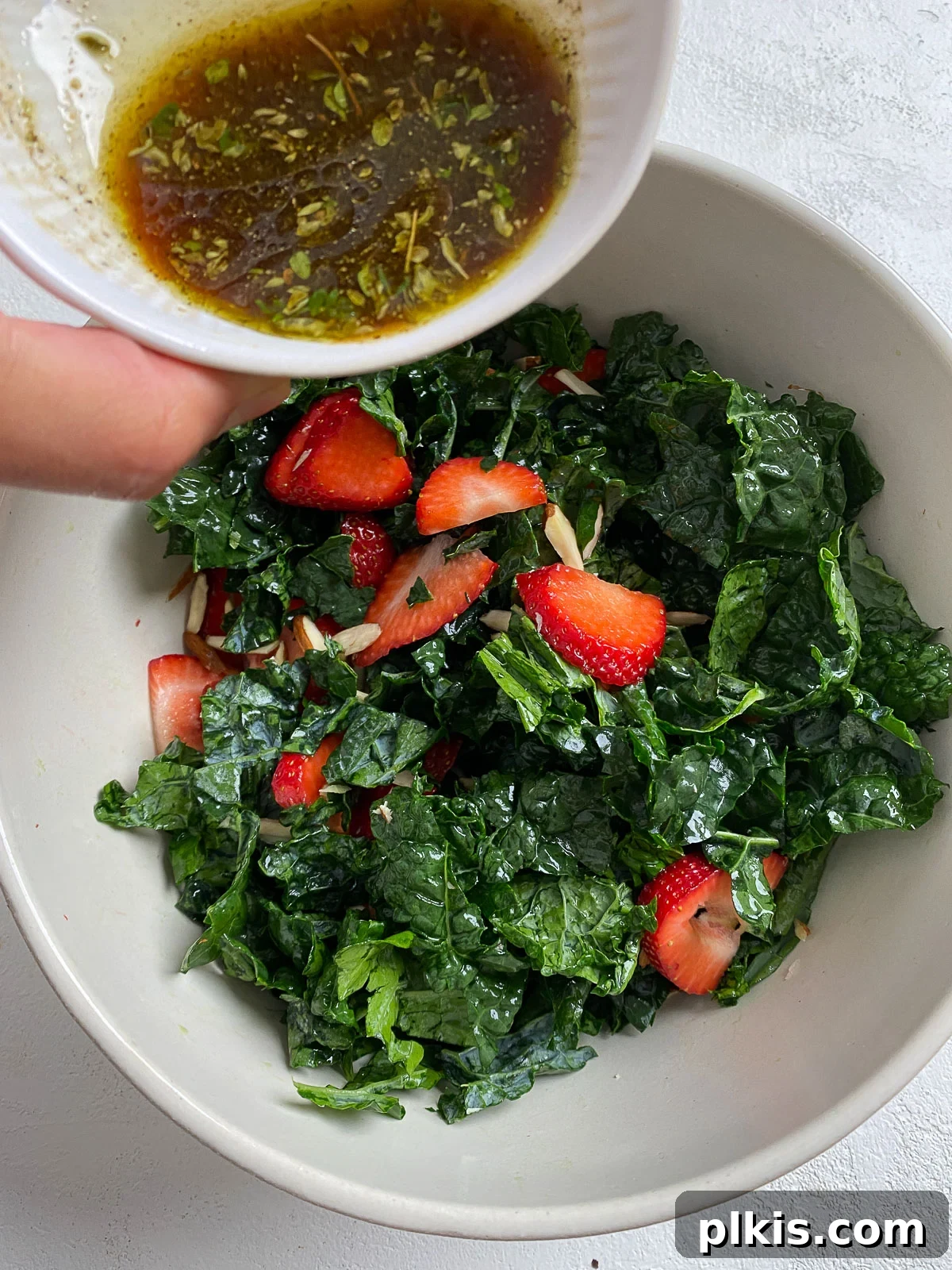 Berry Burst Kale Salad 7 process showing addition of dressing into bowl of strawberry kale salad