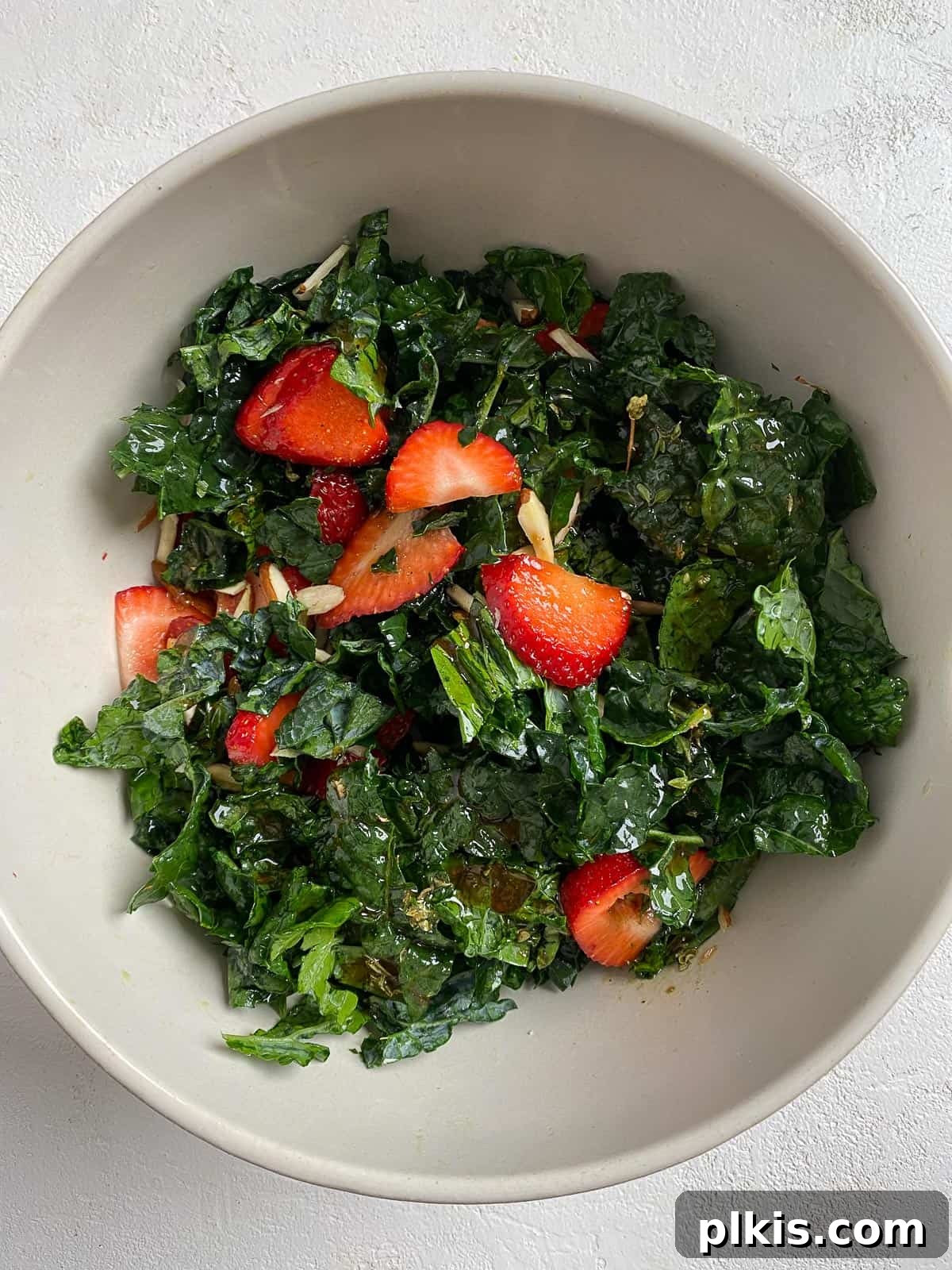 Berry Burst Kale Salad 8 process showing post mixing of dressing into bowl of strawberry kale salad in white bowl, with all ingredients combined