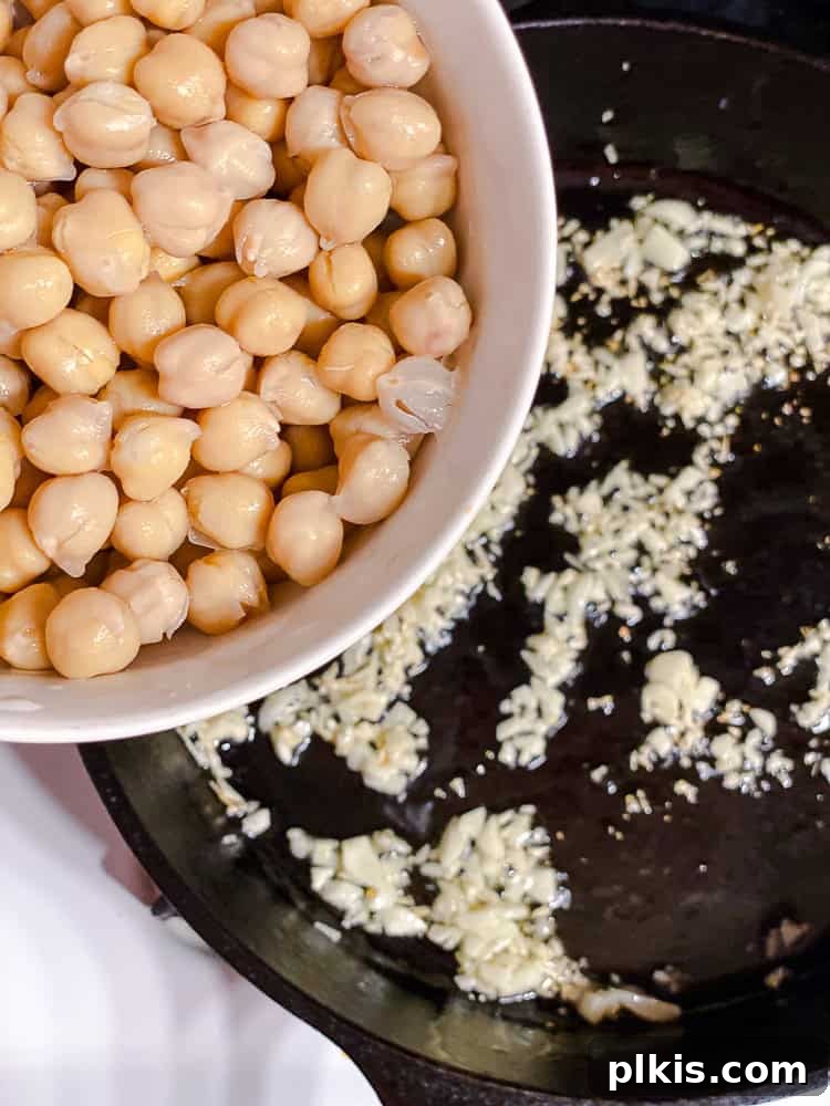 Vibrant Sweet Potato Kale Salad 5 Process shot showing garlic and chickpeas sautéing in a pan.