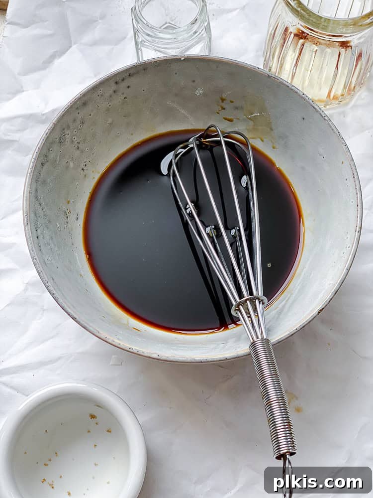 Sweet Chili Glazed Eggplant and Tofu 4 A process shot showing a hand stirring the vibrant soy-garlic sauce in a small bowl, highlighting its rich color and consistency.