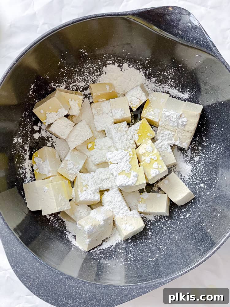 Sweet Chili Glazed Eggplant and Tofu 5 A process shot demonstrating cubed tofu coated in cornstarch in a large mixing bowl, ready for cooking.