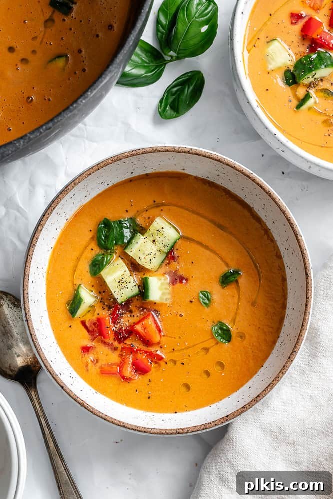 Summer Melon Chill 2 A vibrant bowl of Watermelon Gazpacho, garnished with finely chopped cucumbers, fresh basil leaves, and diced red peppers, presented on a rustic surface.