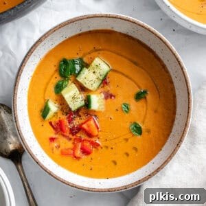 A bowl of Watermelon Gazpacho with chopped cucumbers, basil, and red peppers on top.