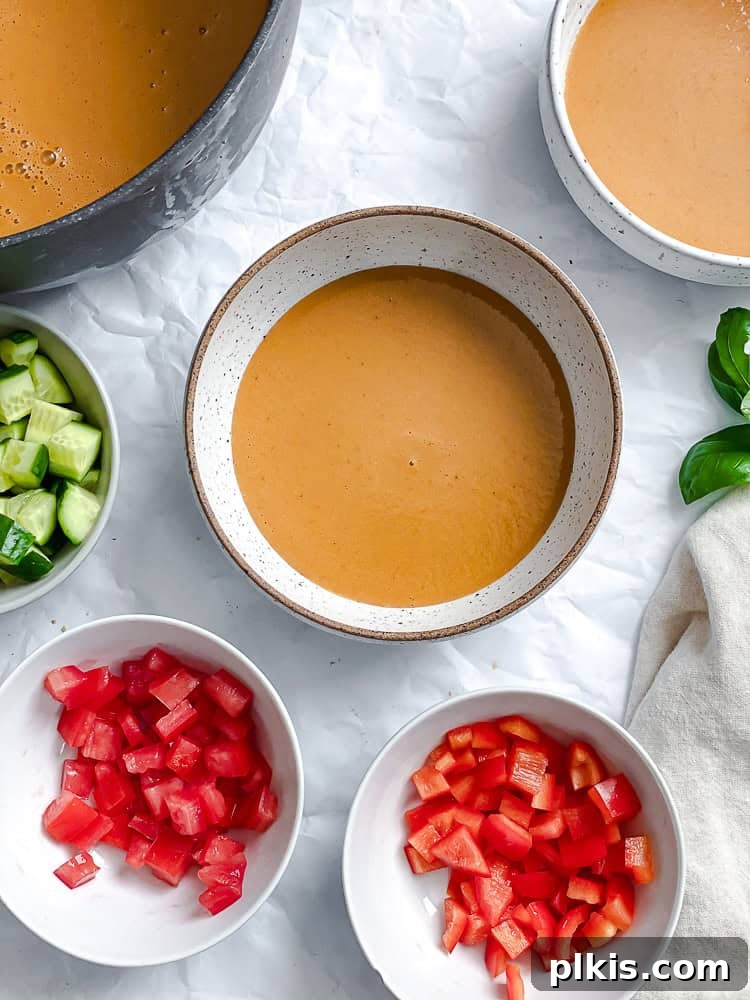 Summer Melon Chill 7 A bowl of chilled Watermelon Gazpacho, elegantly presented with small bowls of fresh chopped tomatoes, red bell peppers, and cucumbers for garnish, signifying readiness to serve.