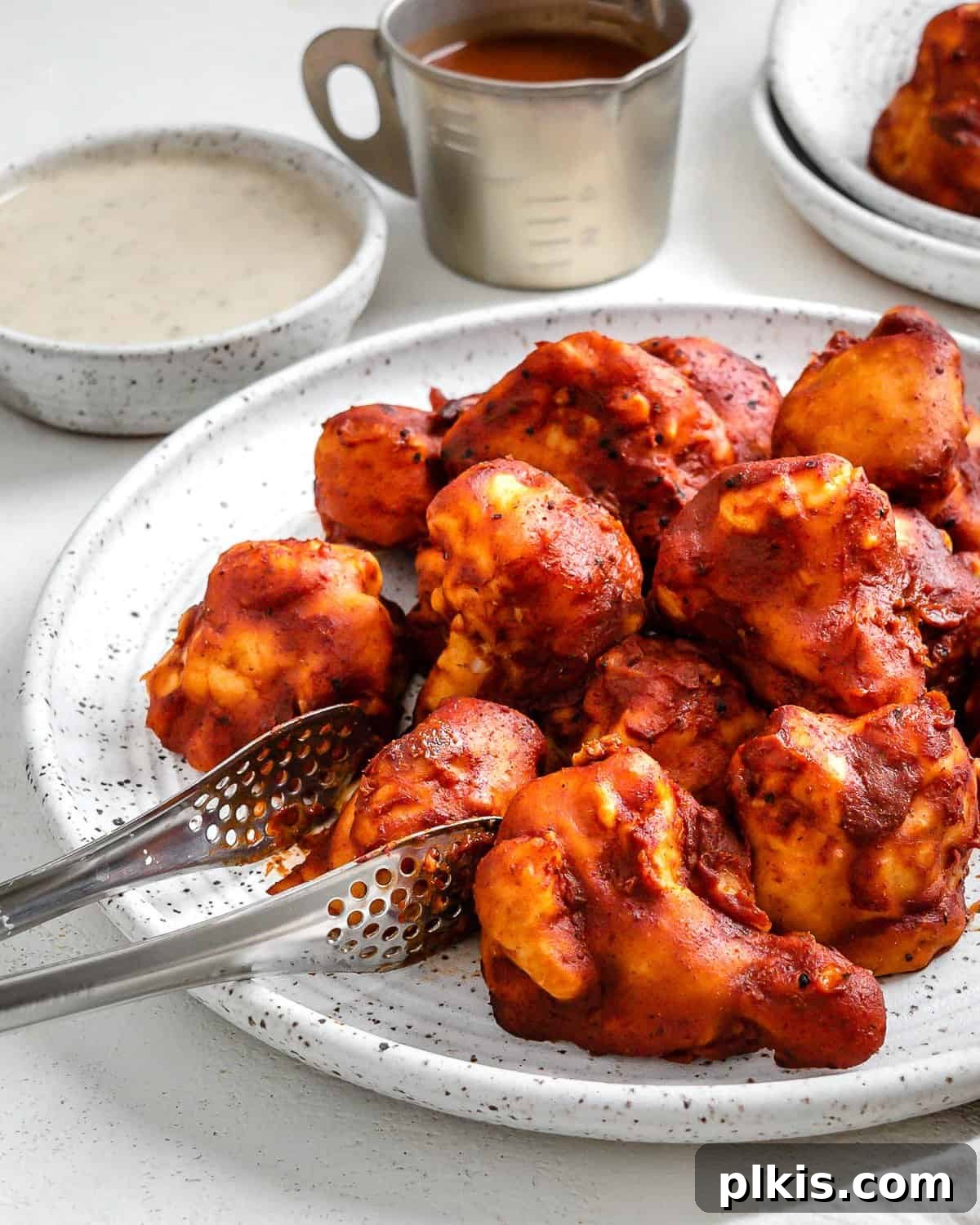 Completed BBQ Cauliflower Wings plated on a white plate with a bowl of sauce in the background