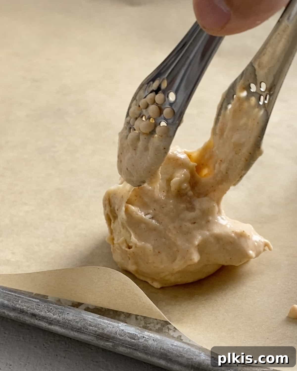 Process shot of placing a cauliflower floret with batter on parchment paper with tongs