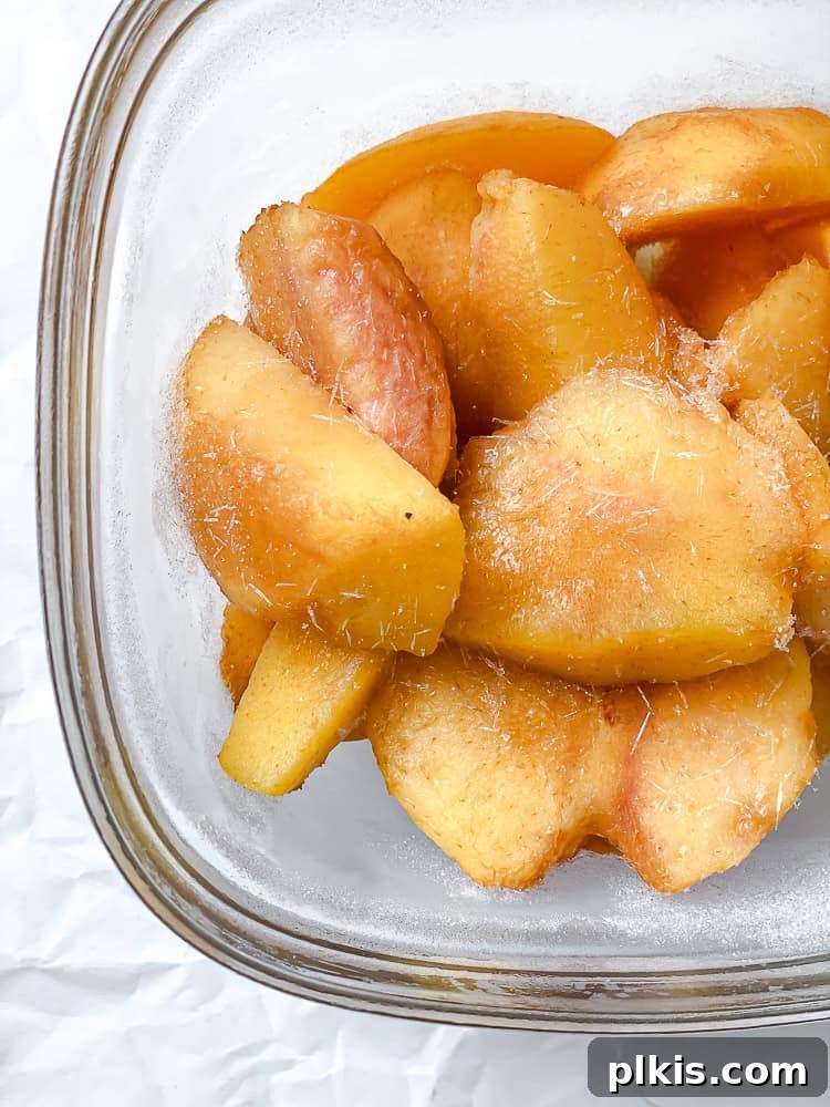 Golden Peach Dream 4 Peeled and sliced fresh peaches are neatly arranged in a clear glass freezer-safe container, ready to be frozen.