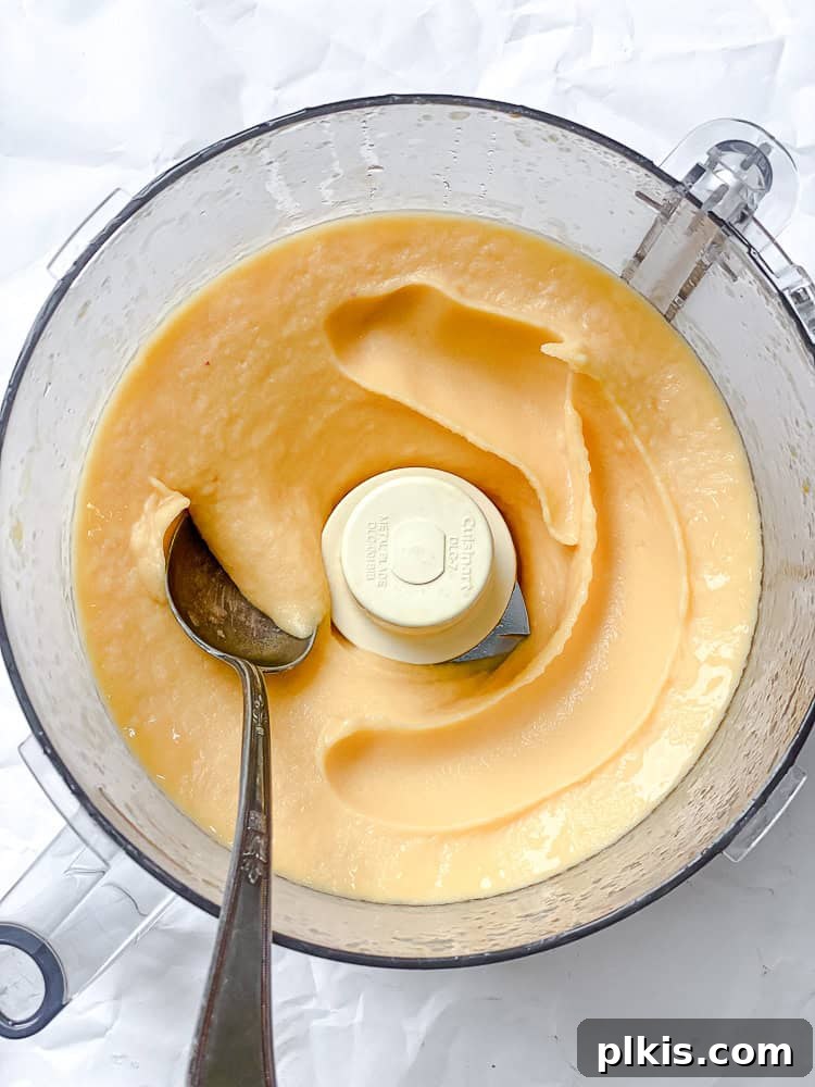 Golden Peach Dream 6 A spoon is used to scoop a swirl of freshly blended peach sorbet from a food processor bowl, showing its smooth, creamy texture and readiness to serve.