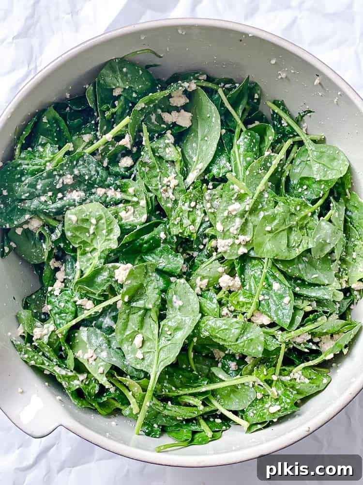 spinach mixed with tofu feta in a large white bowl.