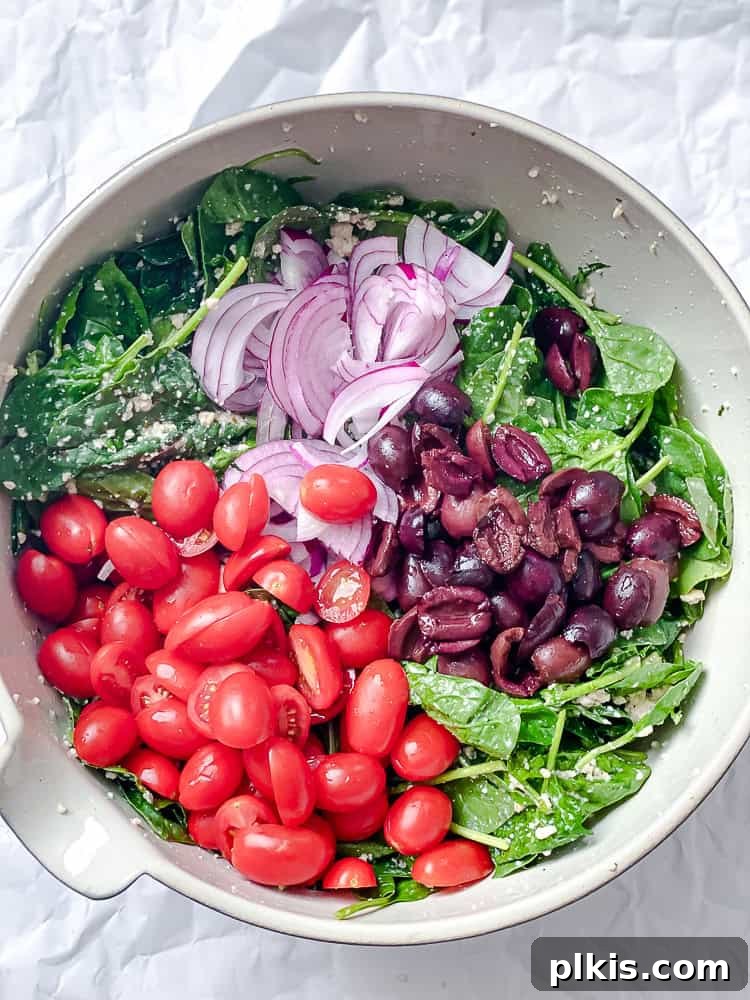 tomatoes, onion, and olives on top of spinach in a large bowl.