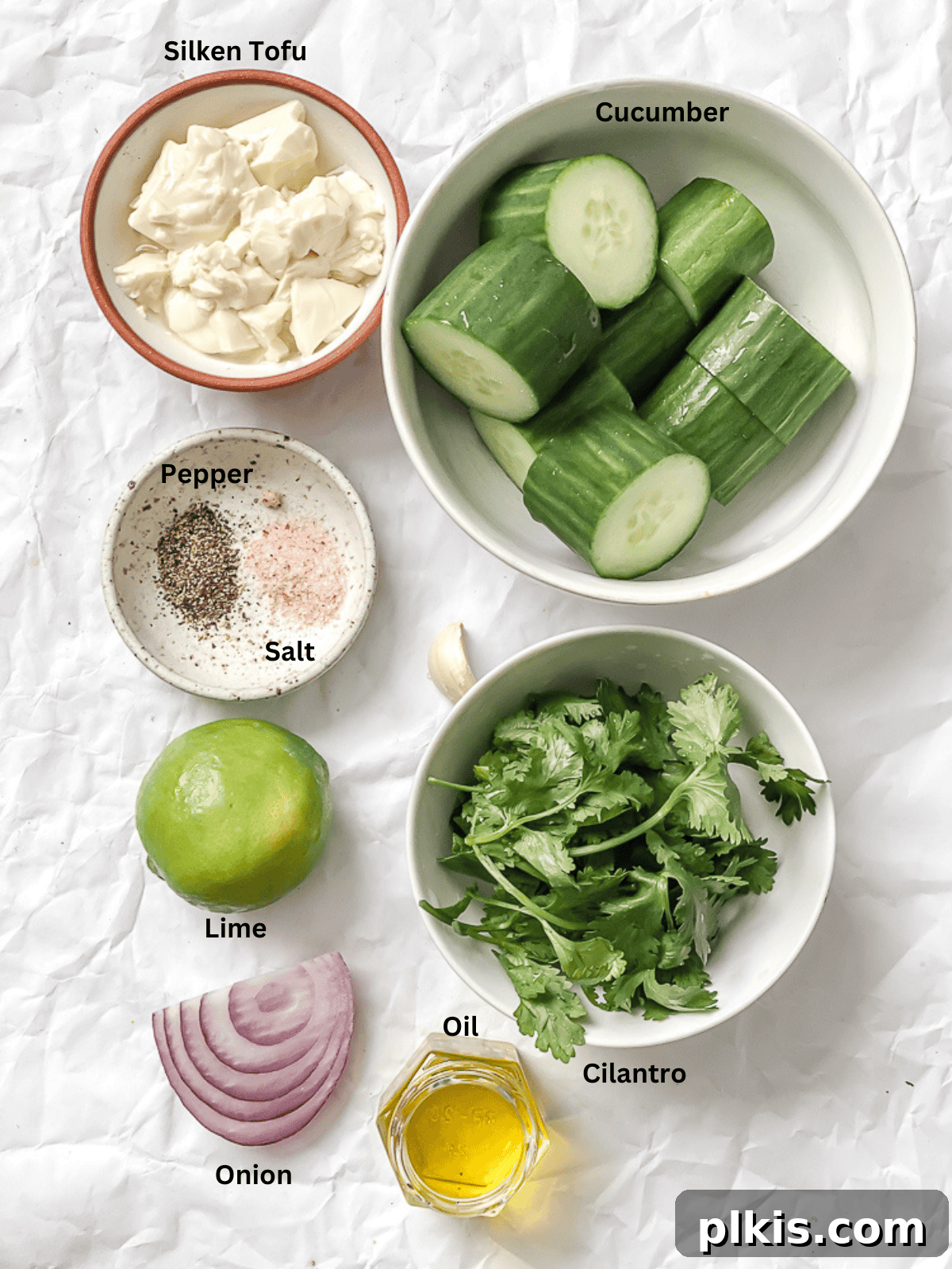 Cool Cucumber Delight 3 A selection of fresh ingredients for Cucumber Gazpacho, including cucumbers, red onion, garlic, cilantro, and lime, laid out on a white surface.