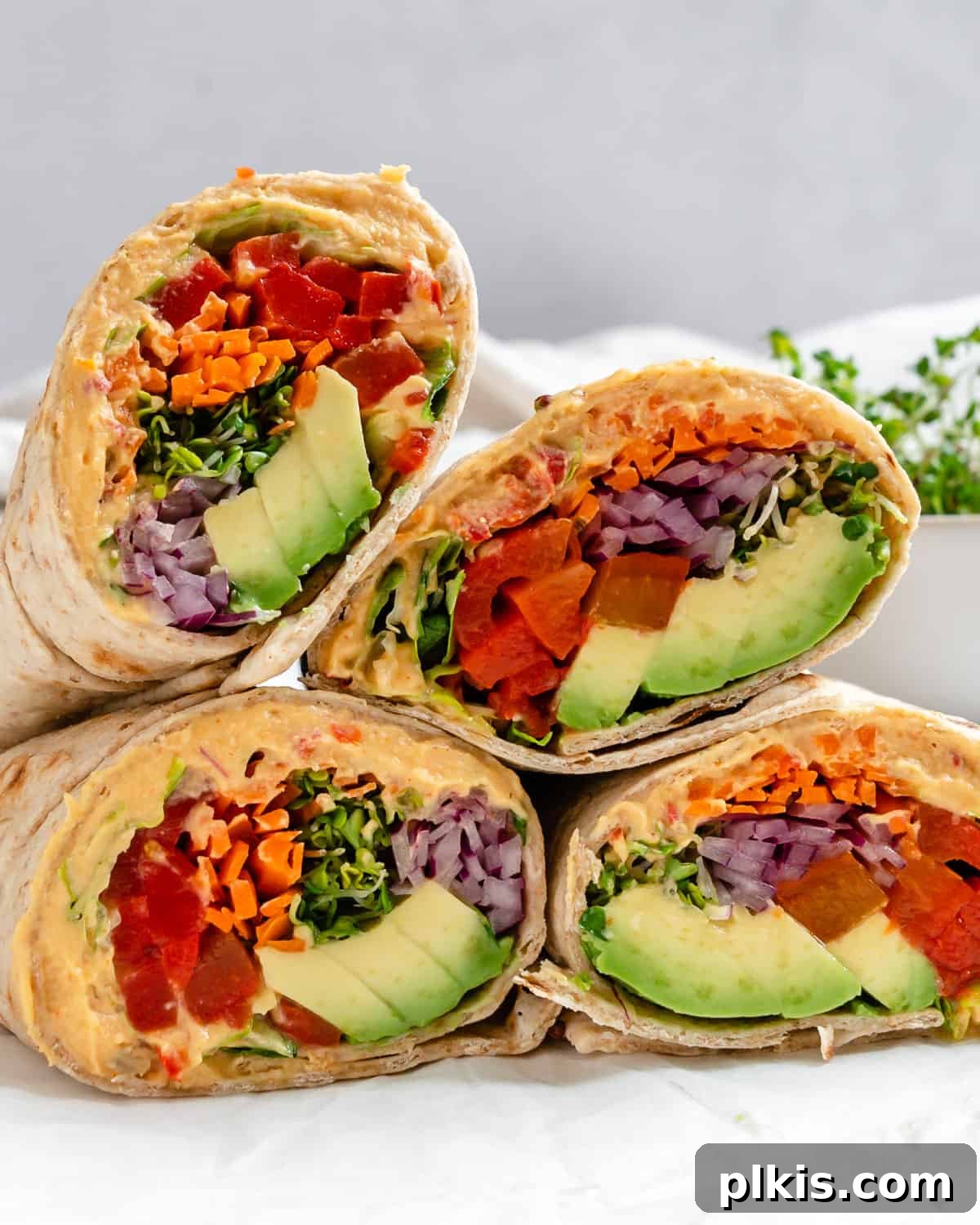 Effortless Hummus Roll Ups 2 Several completed Easy Hummus Tortilla Wraps arranged appealingly on a clean white surface, showcasing their fresh ingredients and vibrant colors.