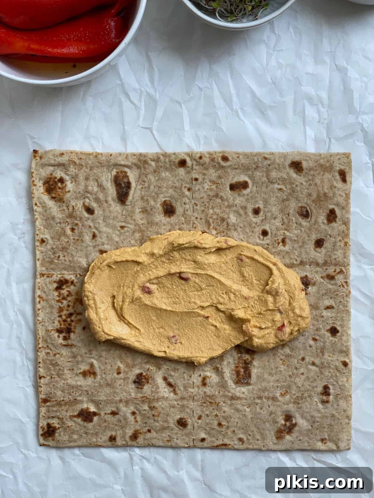 Effortless Hummus Roll Ups 4 Close-up process shot demonstrating hummus being smoothly spread across a tortilla wrap with a spoon, showing an even layer near the center.