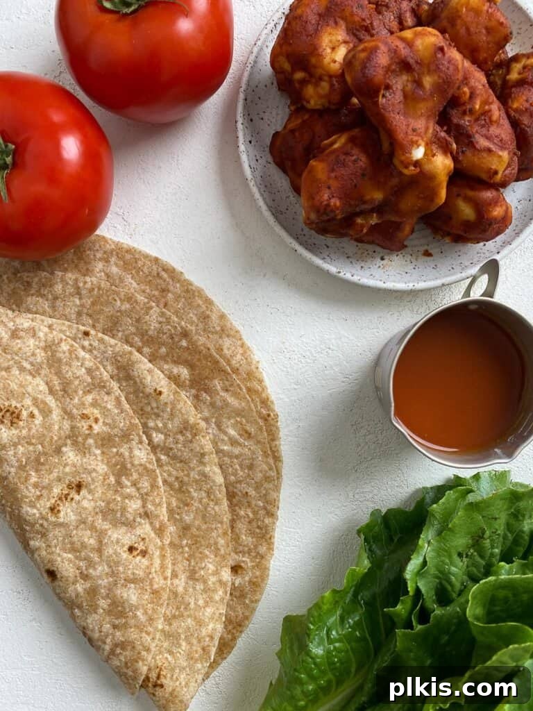 Flavor-Packed Cauliflower Wraps BBQ or Buffalo 3 Assortment of fresh ingredients laid out on a white surface, including BBQ cauliflower bites, romaine lettuce, sliced tomatoes, tortillas, and BBQ sauce, ready for making delicious veggie wraps.