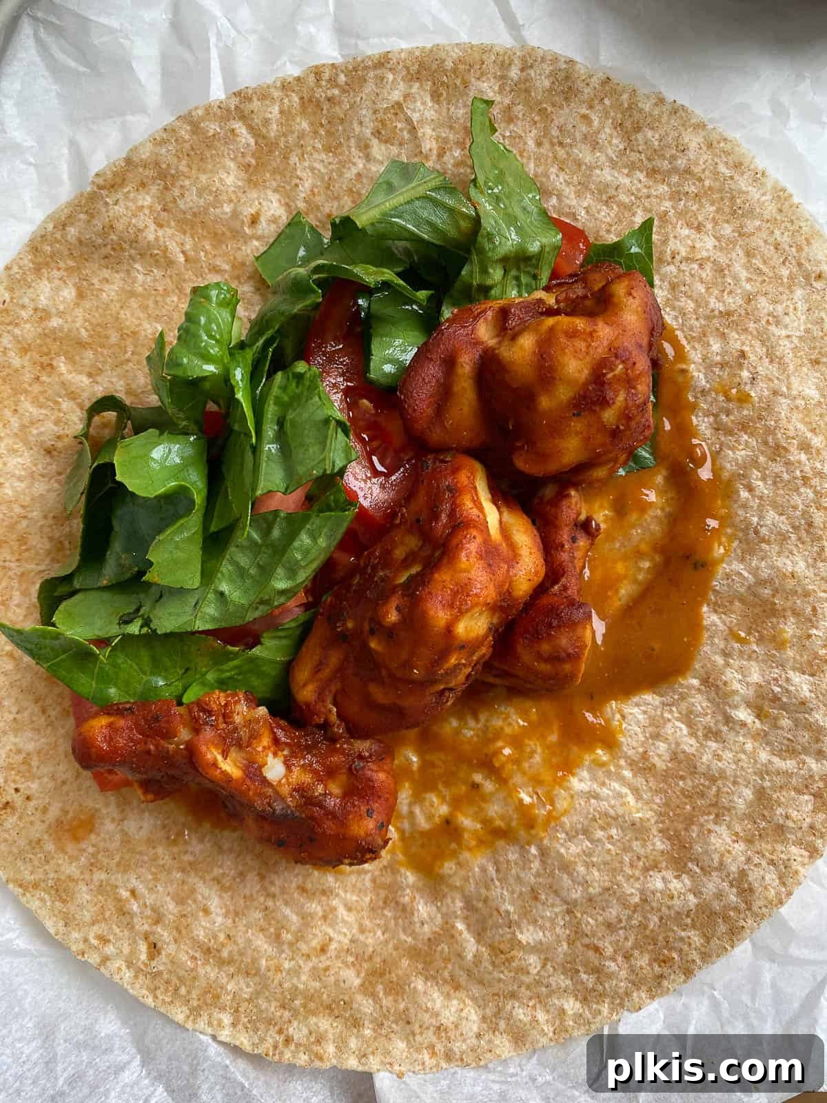 Flavor-Packed Cauliflower Wraps BBQ or Buffalo 7 Process shot of assembling a vegan wrap, showcasing crispy cauliflower bites and fresh green spinach being added onto a tortilla spread with BBQ sauce.