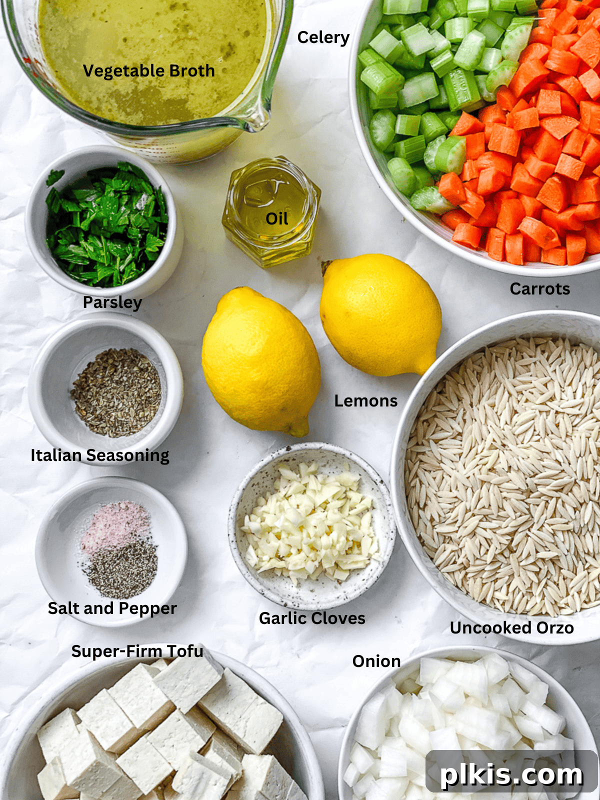 Sunshine Lemon Orzo Soup 3 A spread of fresh ingredients for Lemon Orzo Soup, including olive oil, diced celery, carrots, onion, garlic, vegetable broth, Italian seasoning, tofu, uncooked orzo, and fresh lemons, on a white surface.