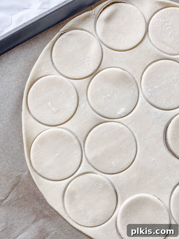 Spiced Apple Pie Cookies 4 Process shot showing a rollout pie crust being cut into mini circles with a round cookie cutter, on a floured surface.