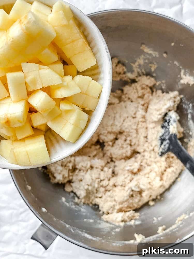 Spiced Apple Pie Cookies 6 Process shot showing finely diced apples being added to a mixing bowl with cookie dough ingredients, ready to be folded in.