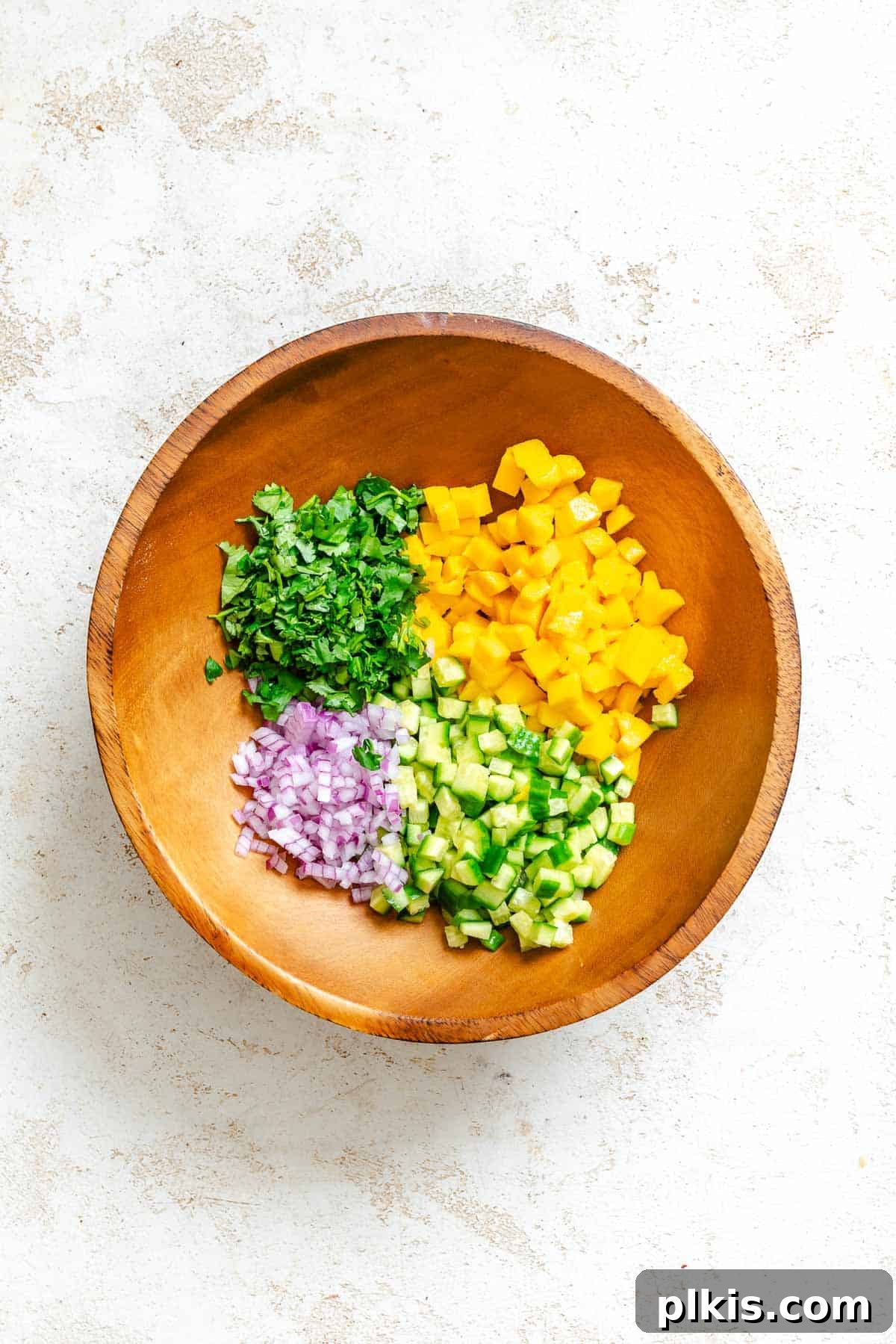 Sunshine Mango Cucumber Salsa 4 Process shot showing ingredients added to a large mixing bowl, vibrant and fresh.