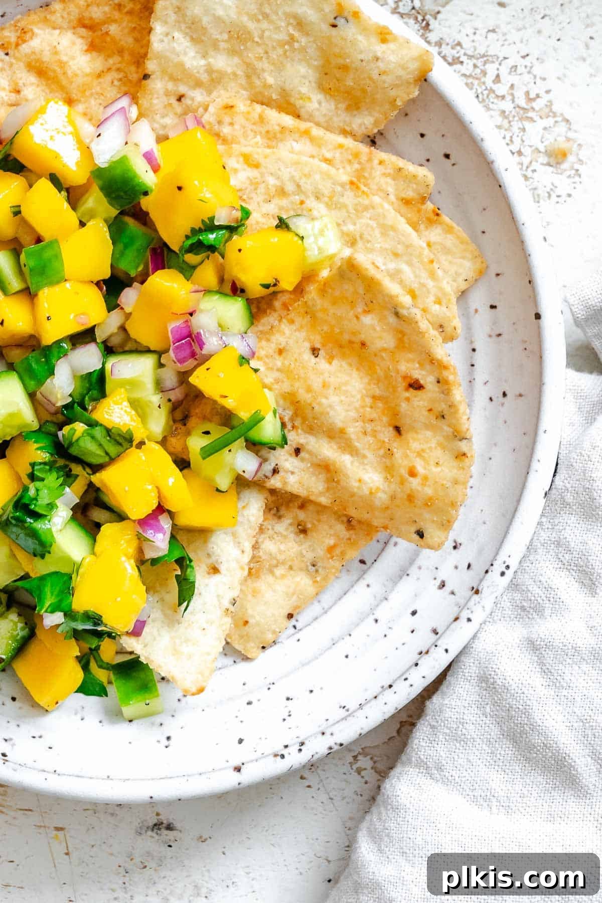 Sunshine Mango Cucumber Salsa 6 Completed Mango Cucumber Salsa on a plate against a white surface, garnished with fresh cilantro.