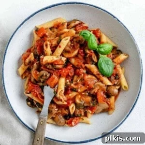 Completed Spicy Tomato Basil Pasta in a white plate against a white surface, garnished with fresh basil.