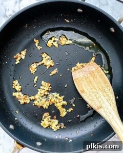 Fiery Basil Tomato Delight 4 Process of garlic and red pepper flakes being sautéed in olive oil in a black pan until golden.