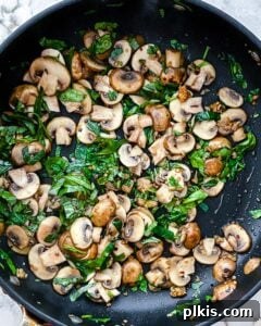 Fiery Basil Tomato Delight 5 Process of mushrooms and greens (basil and spinach) being cooked in a black pan until softened.