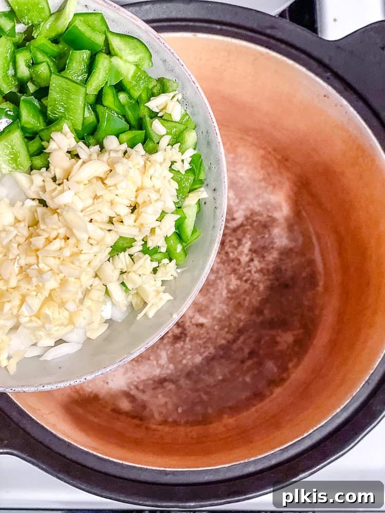 Process shot of adding diced onions, bell pepper, and garlic to a hot pot with oil.