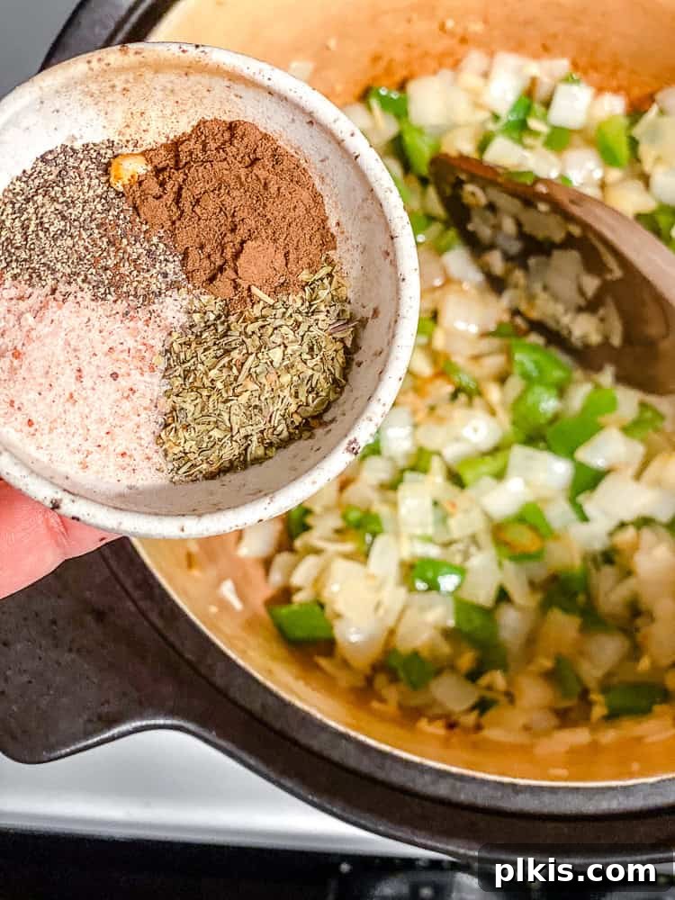 Process shot of adding spices like allspice and Italian seasoning to sautéed vegetables in a pot.