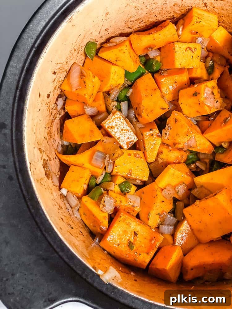 Process shot of adding cubed pumpkin, coconut milk, and vegetable stock to the sautéed ingredients in the pot.