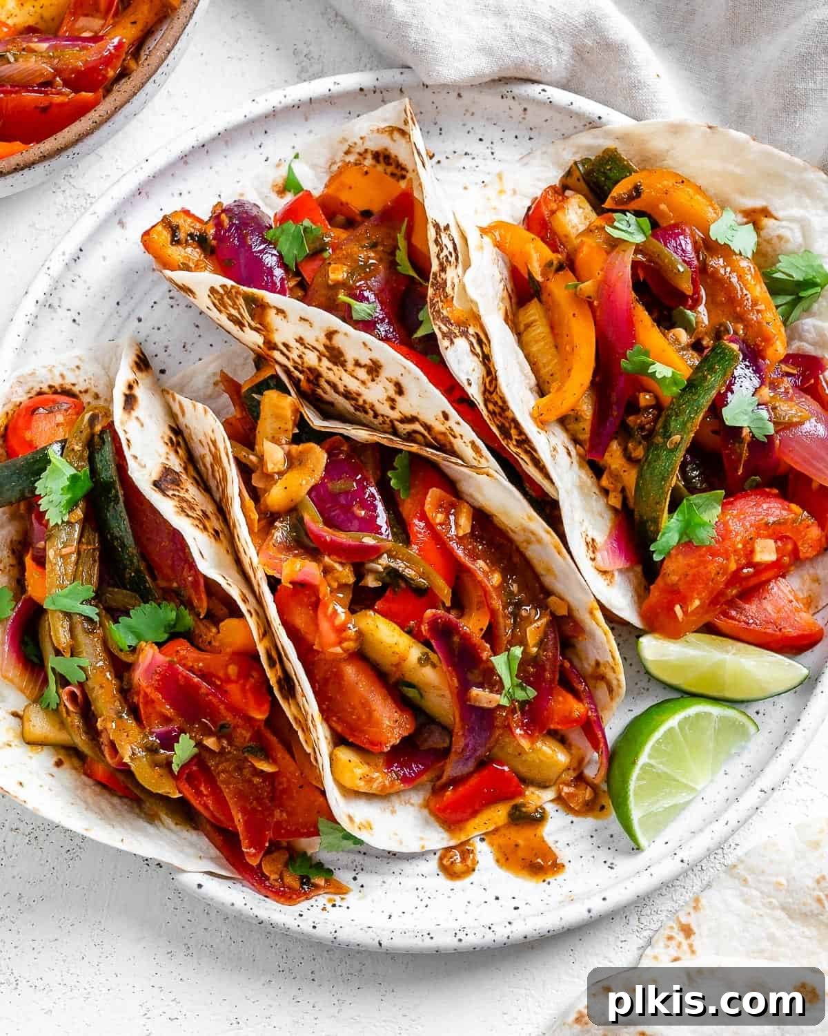 Sizzling Plant-Powered Fajitas 2 completed Grilled Veggie Fajitas on a white speckled plate with veggies in the background