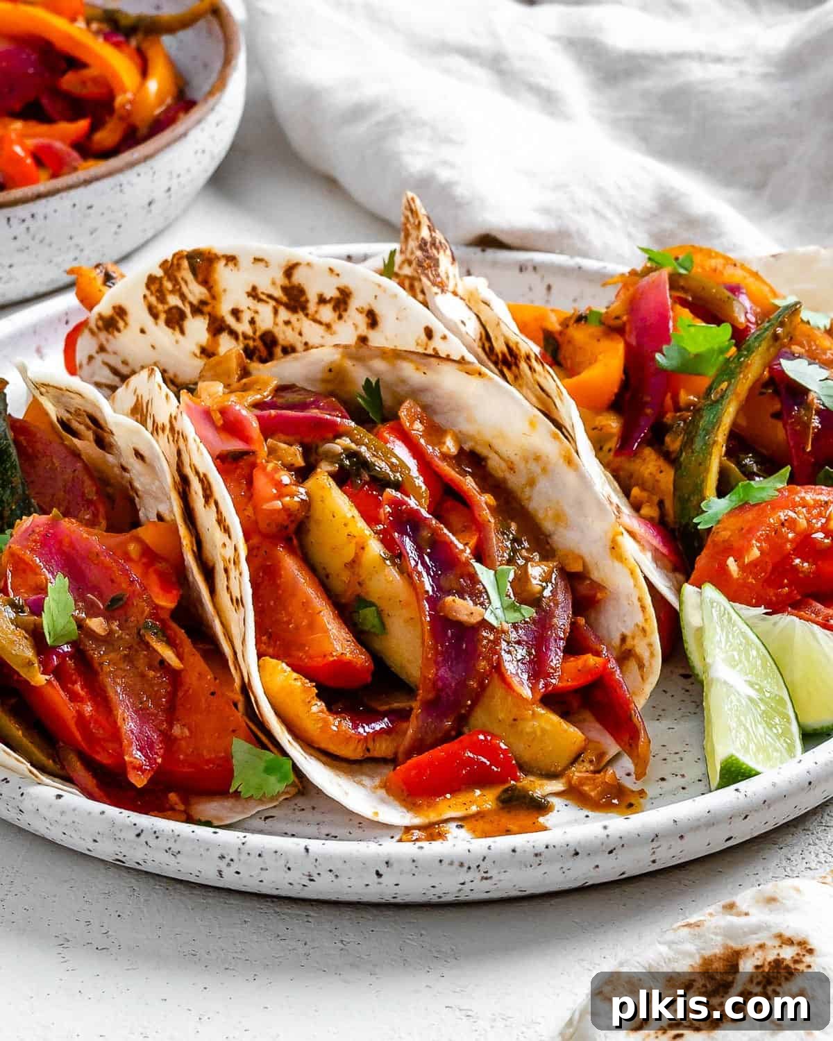 Sizzling Plant-Powered Fajitas 12 completed Grilled Veggie Fajitas on a white speckled plate with veggies in the background