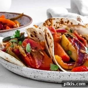 Sizzling Plant-Powered Fajitas 13 completed Grilled Veggie Fajitas on a white speckled plate with veggies in the background