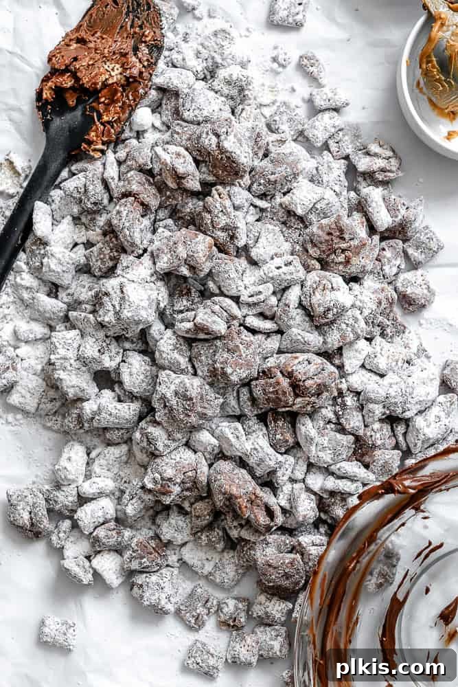 A vibrant bowl of completed Easy Muddy Buddies [Puppy Chow] featuring golden Chex cereal coated in rich chocolate peanut butter and dusted with powdered sugar, resting on a clean white surface, invitingly ready to be enjoyed.