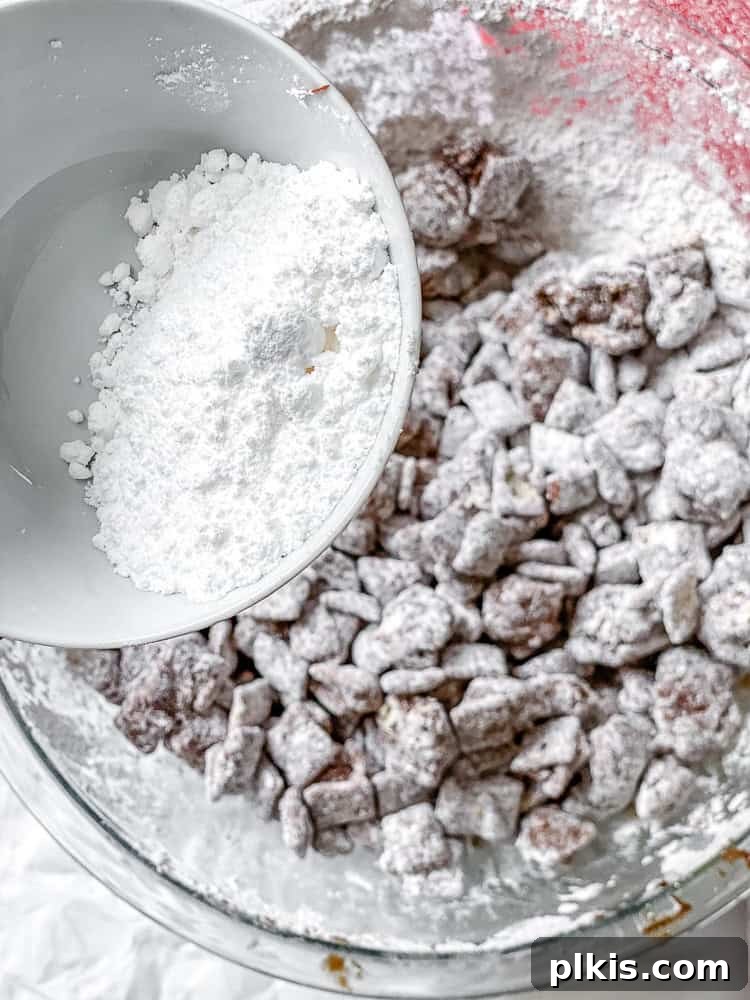 Simple Homemade Puppy Chow 6 Process shot capturing the moment powdered sugar is added to the bowl of chocolate-coated Chex cereal, illustrating the beginning of the final dusting step for Easy Muddy Buddies.