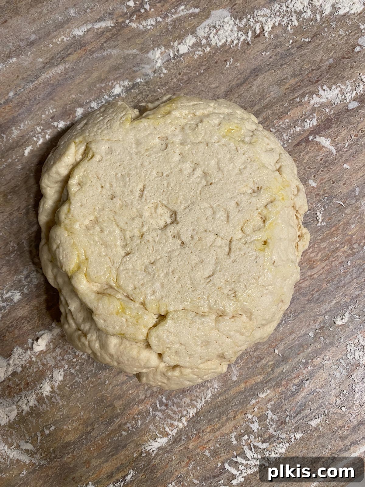 The proofed pizza dough, punched down and ready to be rolled out on a floured surface, showcasing its soft texture.