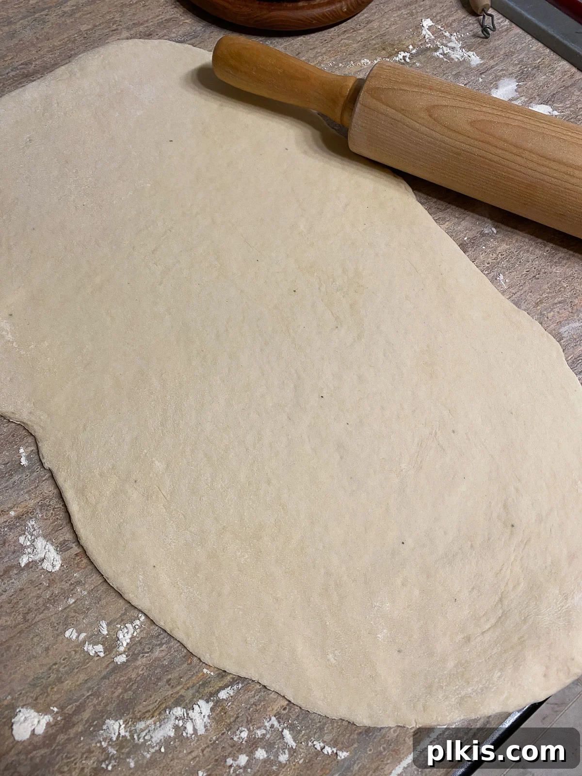 A rolling pin flattening the pizza dough into a large, even rectangle on a countertop, ready for toppings.