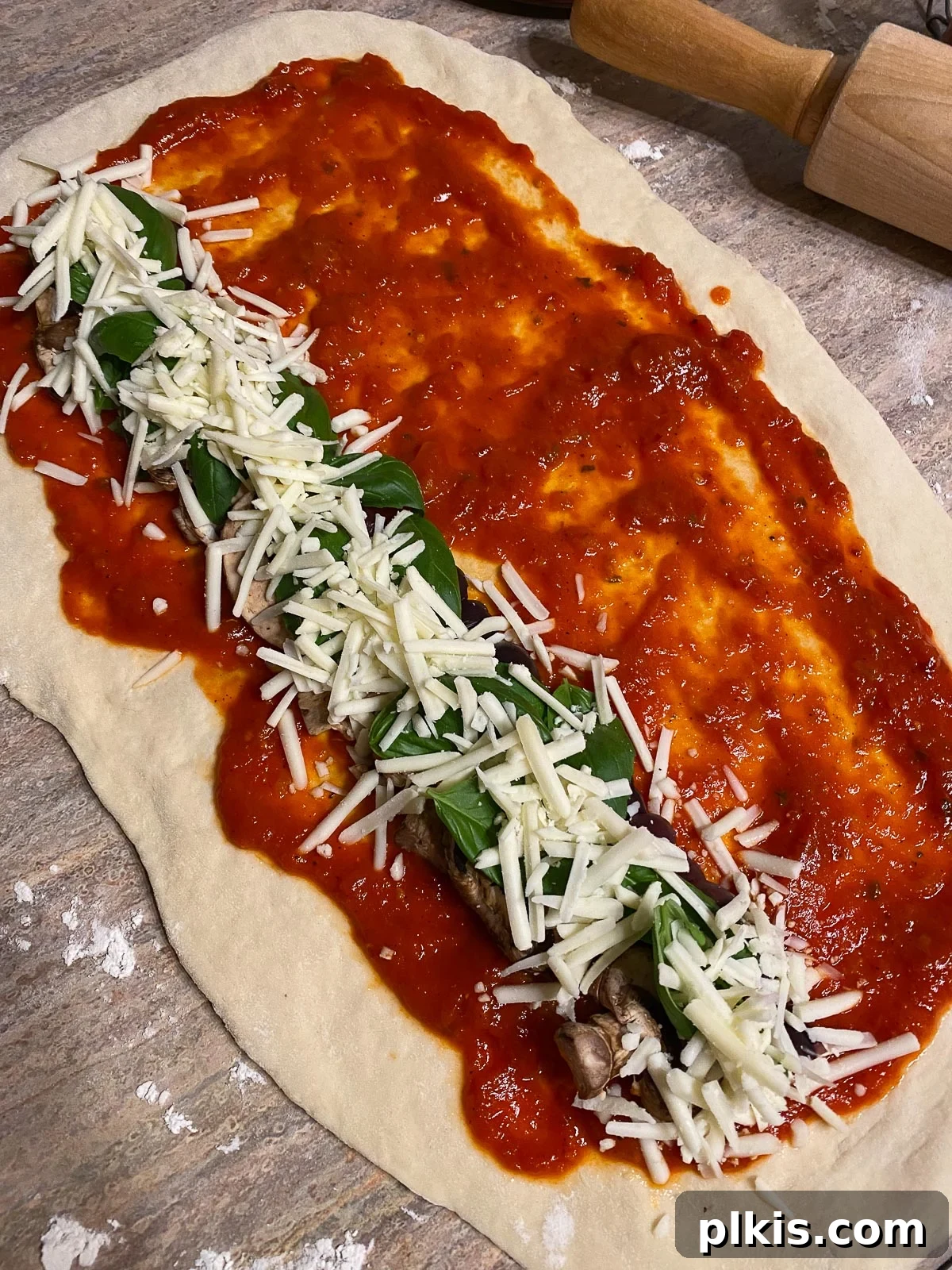 The rolled-out pizza dough generously covered with marinara sauce, chopped basil, and vegan cheese, ready to be rolled up.