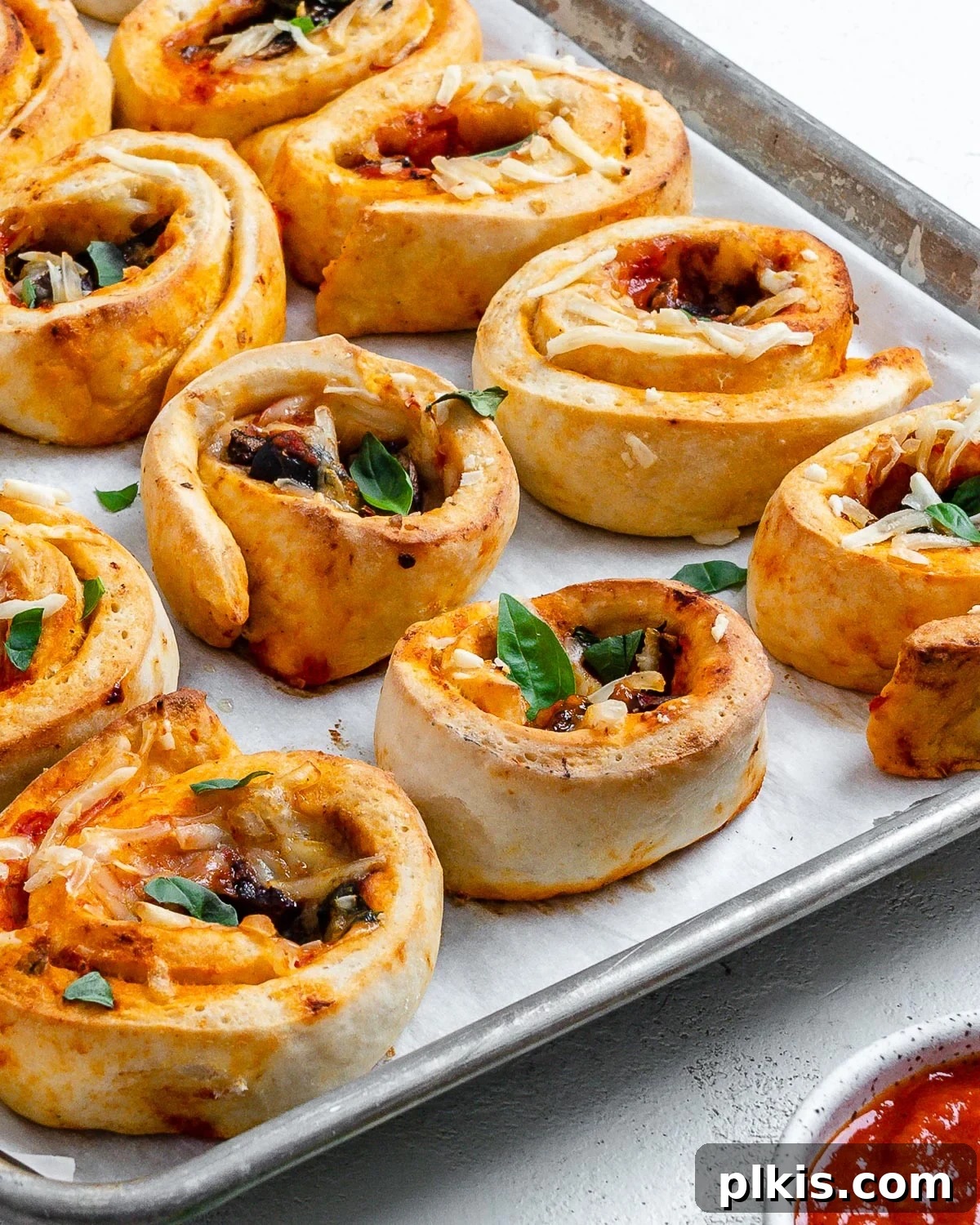 A vibrant close-up of several perfectly baked vegan pizza rolls on a baking dish, displaying their golden crusts and colorful toppings.
