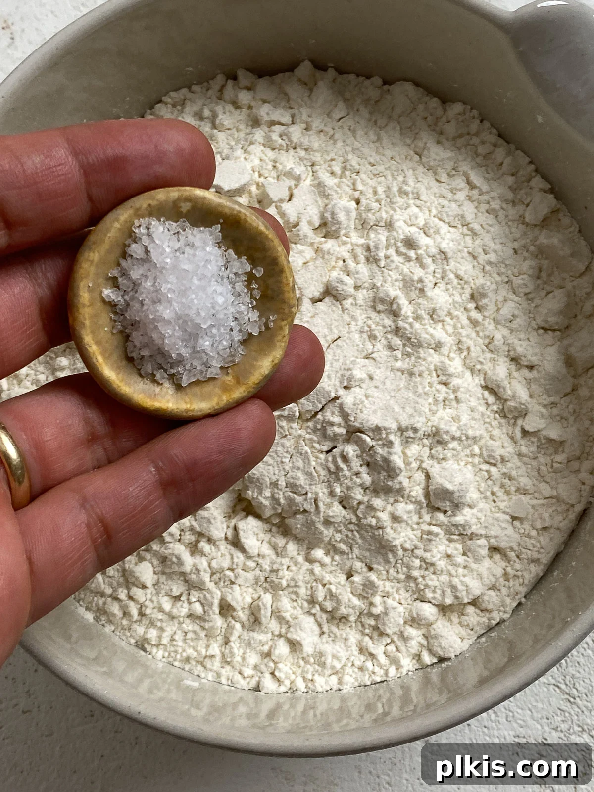 A bowl of flour with salt being added, demonstrating the initial combination of dry ingredients for the pizza dough.