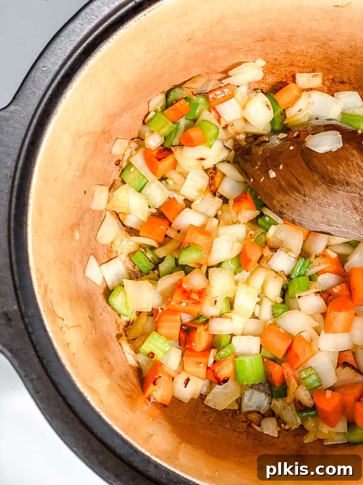 Sunshine Lentil Soup 5 Process shot showing a wooden spoon stirring sautéed vegetables in a pot, having just added spices like cumin and Italian seasoning.
