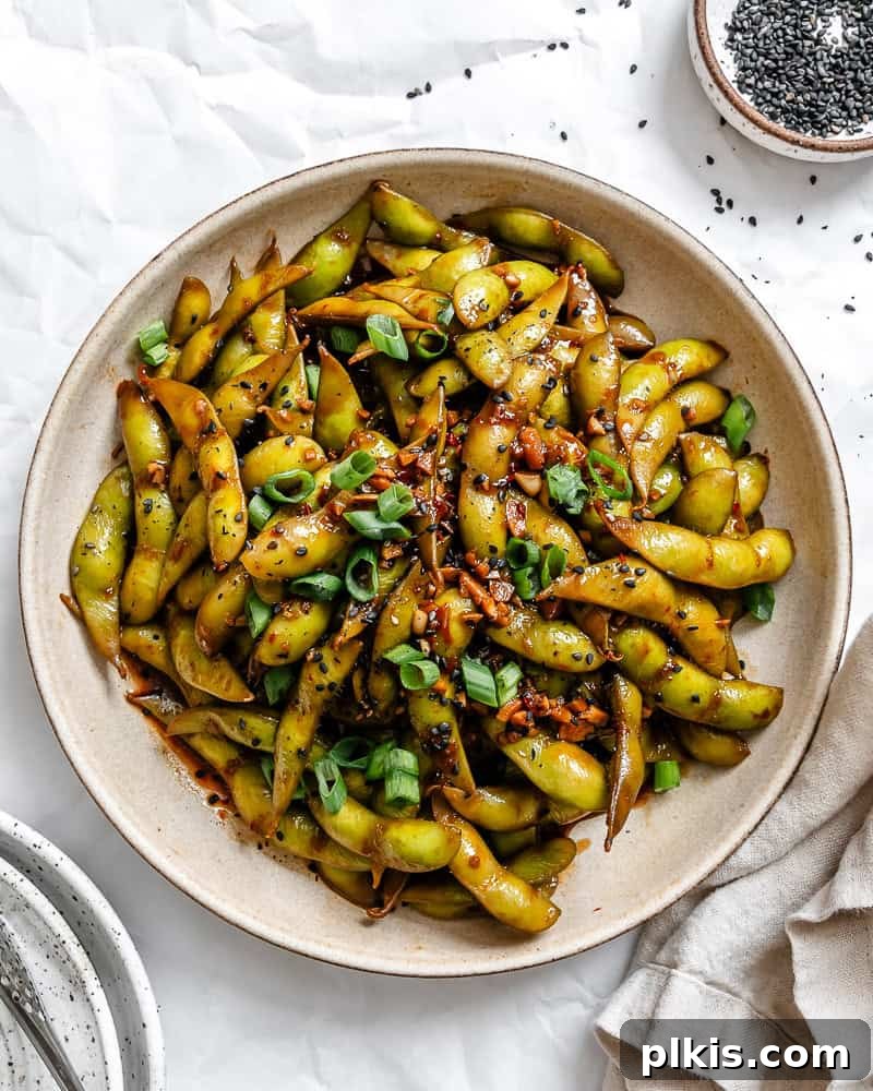 A plate of freshly prepared Quick Spicy Edamame [Chili and Garlic], vibrant green pods coated in a rich, fiery sauce.
