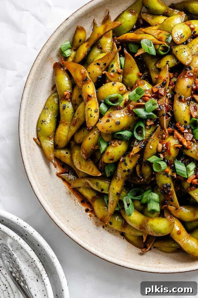 Close-up shot of the finished Quick Spicy Edamame [Chili and Garlic] served on a white plate, garnished with green onions and sesame seeds.