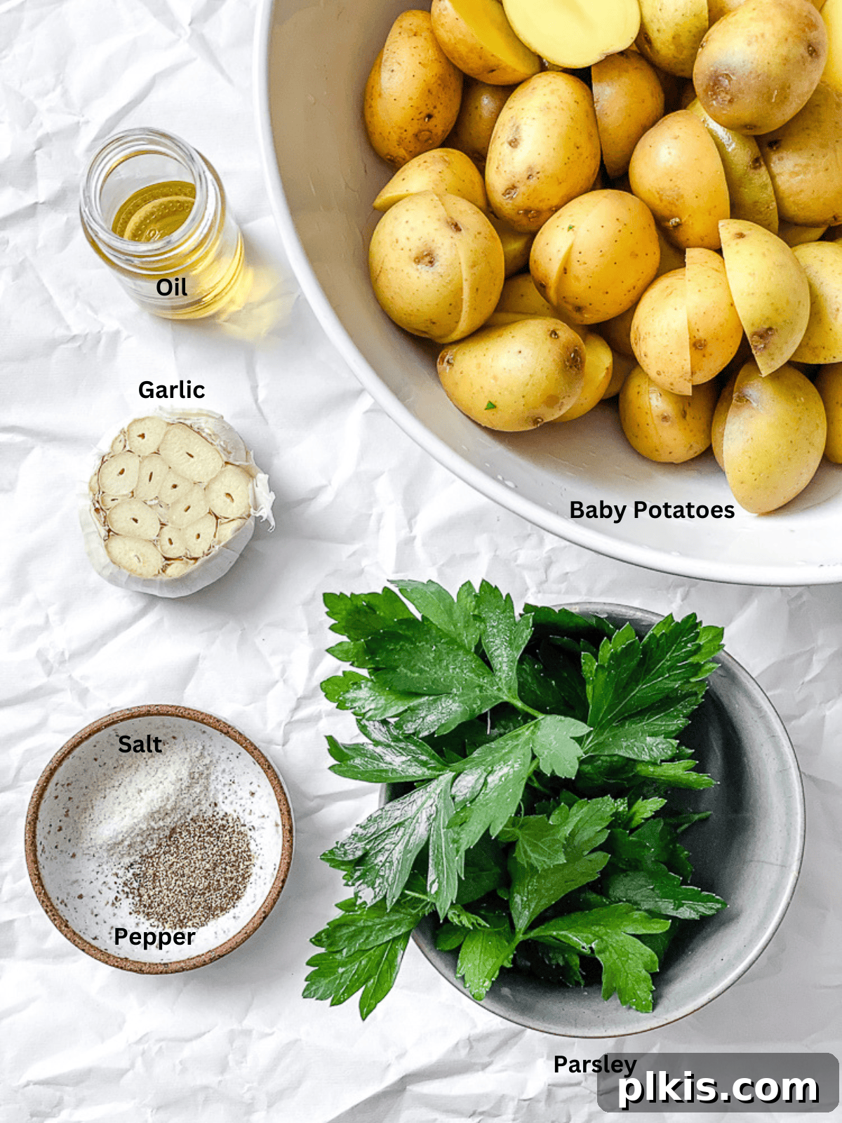 Rosemary Garlic Roasted Baby Potatoes 2 Fresh ingredients for Garlic Roasted Baby Potatoes laid out on a white surface, including baby potatoes, garlic, parsley, and olive oil.